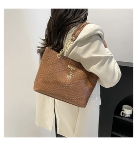 Close-up of brown woven tote bag with gold chain strap and deer charm on a model