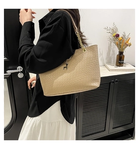 Detail of woven textured shoulder bag with chain strap and deer pendant on model