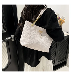 Detail of white tote bag featuring scale texture, gold chain and deer charm on a model