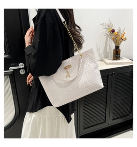 Close-up of white woven tote bag with slim handles, gold chain, and deer pendant detail