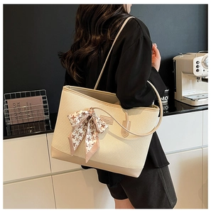 Detail of beige woven tote bag with silk scarf accent and logo on shoulder of a model
