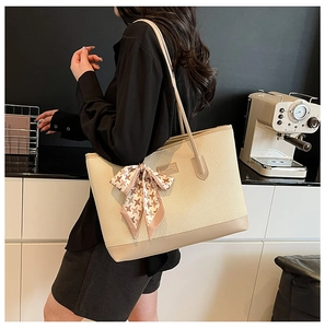 Detail of a large woven tote bag with leather trim and a houndstooth ribbon bow