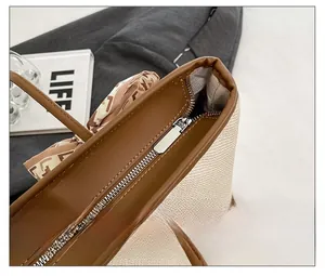 Close-up of beige woven tote bag with brown leather trim, silver zipper, and silk scarf
