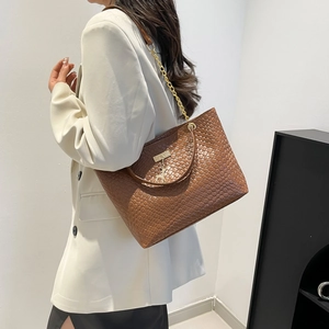 Brown woven PU leather tote bag with gold deer charm shown on shoulder with white blazer