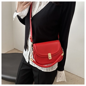 Detailed view of a vintage red matte leather saddle bag worn with a black cardigan