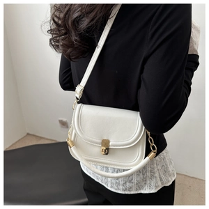 Detail of white matte leather saddle bag with gold buckle and chain handle on model