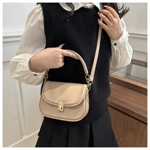 Detail of beige leather saddle bag featuring a gold square twist lock and top handle