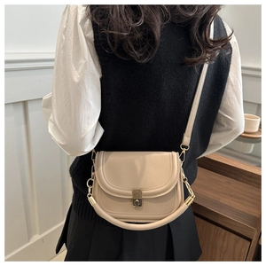Detail of a beige leather saddle bag featuring a gold metal lock and shoulder strap