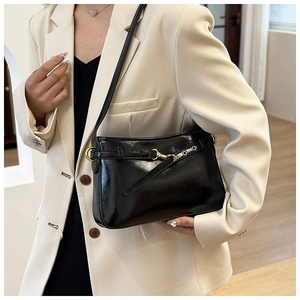 Détail du sac à bandoulière noir brillant avec garnitures dorées sur blazer crème