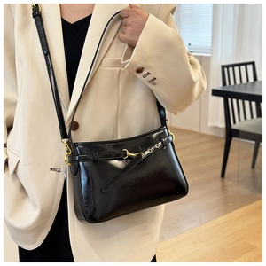 Détail d'un sac à bandoulière noir élégant avec boucles dorées porté sur un blazer