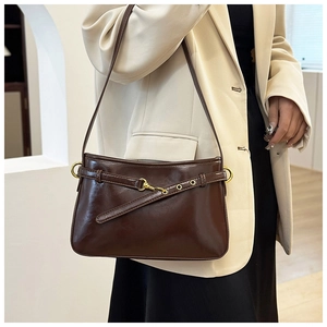 Détail du sac bandoulière en cuir brillant marron foncé avec boucle dorée et œillets