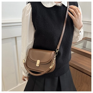 Detail of a brown saddle crossbody bag featuring a vintage gold clasp and leather texture