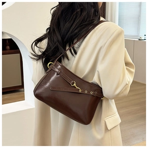 Détail du sac sous le bras en cuir marron café avec boucle dorée sur blazer blanc