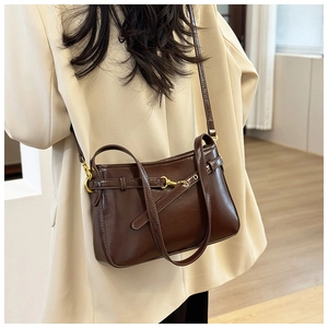 Détail du sac bandoulière en cuir brillant marron foncé avec boucles dorées sur blazer