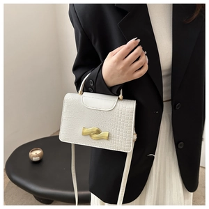 Detail of white crocodile pattern crossbody bag with golden clasp worn by a model