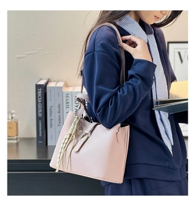 Detail of dusty rose pebbled leather bucket bag with metal buckle and woven charm