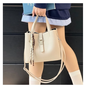 Detail of beige litchi grain bucket bag with top handle and woven tassel ornament