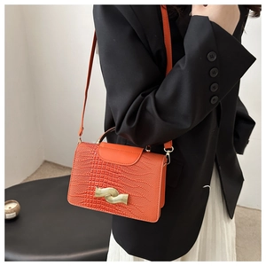 Detail of orange crocodile pattern crossbody bag with golden wave-shaped metal buckle