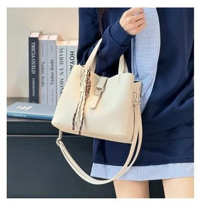 Detail of cream lychee leather bucket bag with metal buckle and decorative scarf