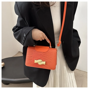 Detail of orange crocodile embossed handbag featuring a unique gold wave-shaped buckle