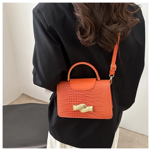 Detail of orange embossed crocodile pattern handbag with golden wavy buckle on black blazer