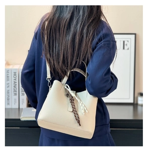 Creamy white lychee grain leather bucket bag shown as a crossbody on a casual model