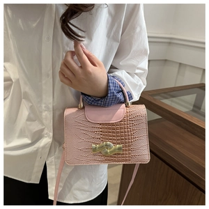 Detail of pink crocodile embossed handbag showing the wavy gold metal clasp and top handle