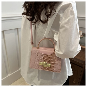 Detail of pink croc-embossed handbag with gold hardware and curved metal handle