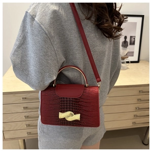 Detail of dark red crocodile pattern handbag with gold hardware and long strap