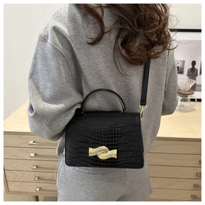 Detail of a black lizard-textured handbag with a gold-tone clasp shown on model