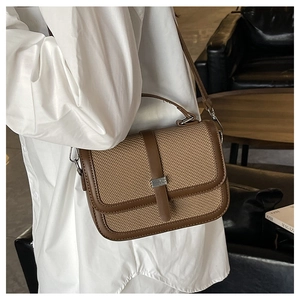 Brown leather and woven crossbody bag styled on a sofa in a modern indoor setting