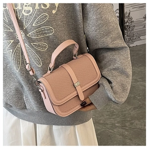 Detail of light pink crossbody bag featuring woven texture and metallic clasp