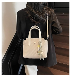 Detail of cream woven handbag with cute bear charm and rounded handles on a model