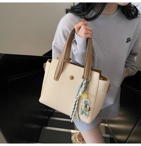 Detail of beige woven bucket bag with brown leather handles and cute bear charm pendant