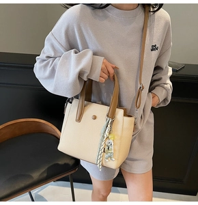 Chic off-white woven tote bag with brown leather handles and scarf charm on model
