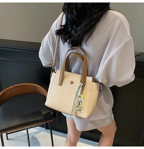 Detail of beige woven tote bag with brown leather handles, green silk scarf and bear charm