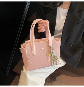 Close-up of pink woven texture handbag with cute bear charm and decorative round buckle