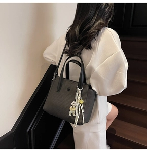 Detail of black woven texture tote bag with leather handles and white puppy charm
