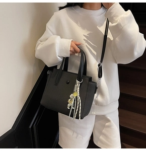 Detail of black textured tote bag with a white bear charm and removable shoulder strap