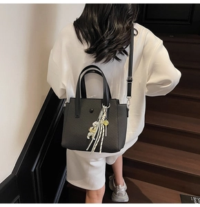 Detail of black woven texture handbag with bear charm and tassel on a model