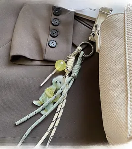 Close-up of curly white dog acrylic charm with green braided rope on a beige leather tote
