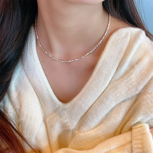 Vue détaillée d'un collier chaîne argentée à facettes porté sur un pull en maille blanc