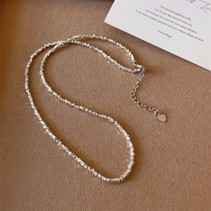 Collier minimaliste en perles argentées avec breloque cœur sur fond en daim marron