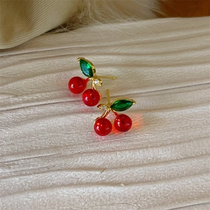 Elegant red cherry stud earrings with gold trim and green leaves on a white textured surface