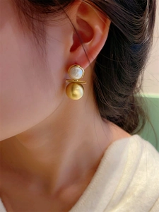 Vue macro de boucles d'oreilles barre dorée avec perle et sphère en métal brossé chic
