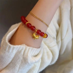 Red agate bead bracelet with golden horse charm worn on a warm knitted background
