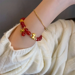 Red agate bead bracelet set with golden kitty and bell charms on a white knit sweater background