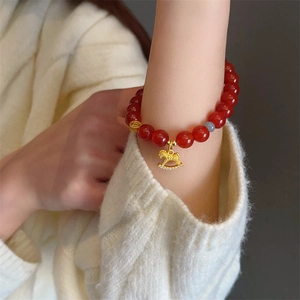 Macro shot of red agate beaded bracelet with golden rocking horse and coin charms