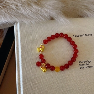 Detail of red agate bead bracelet with golden Pixiu and gourd charms on a white book