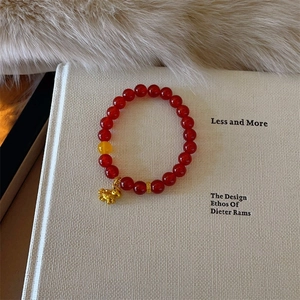 Close-up of red agate beaded bracelet with a golden pig charm on a soft fabric background